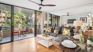 A modern living room with a glass coffee table, a grey sofa with decorative pillows, and a balcony with outdoor furniture.