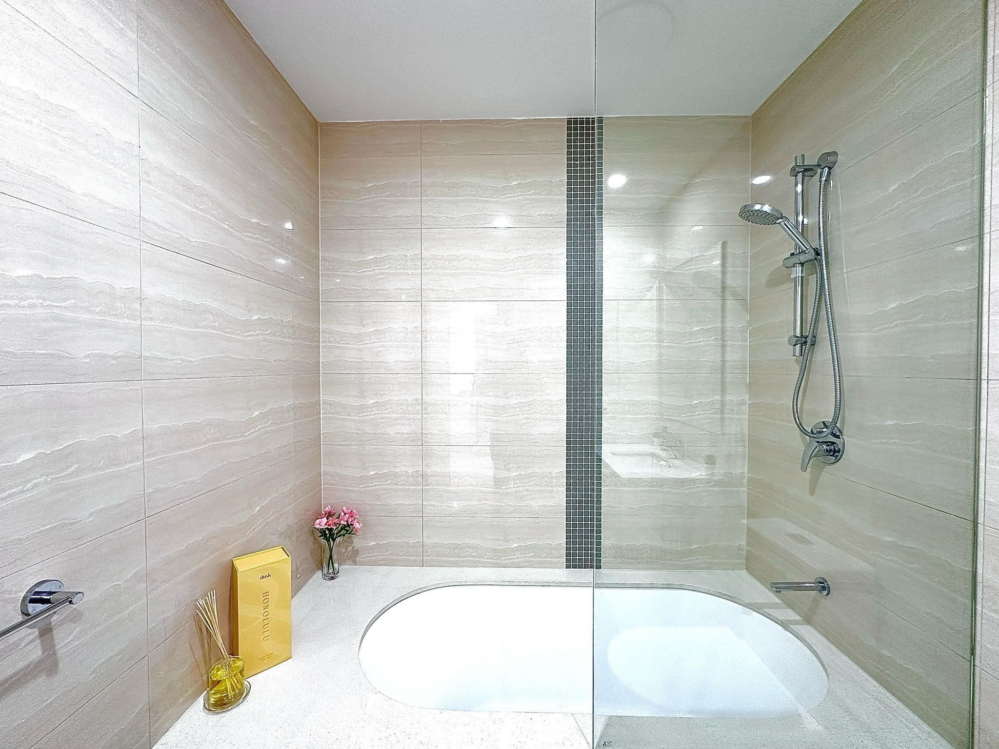 A modern bathroom with a freestanding bathtub, a shower with a handheld showerhead, and a small vase with flowers on the vanity.
