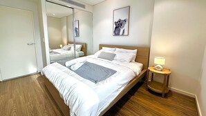 Een moderne hotelkamer met een groot bed, een nachtkastje met een lamp, een spiegel en een lijst met een afbeelding aan de muur.