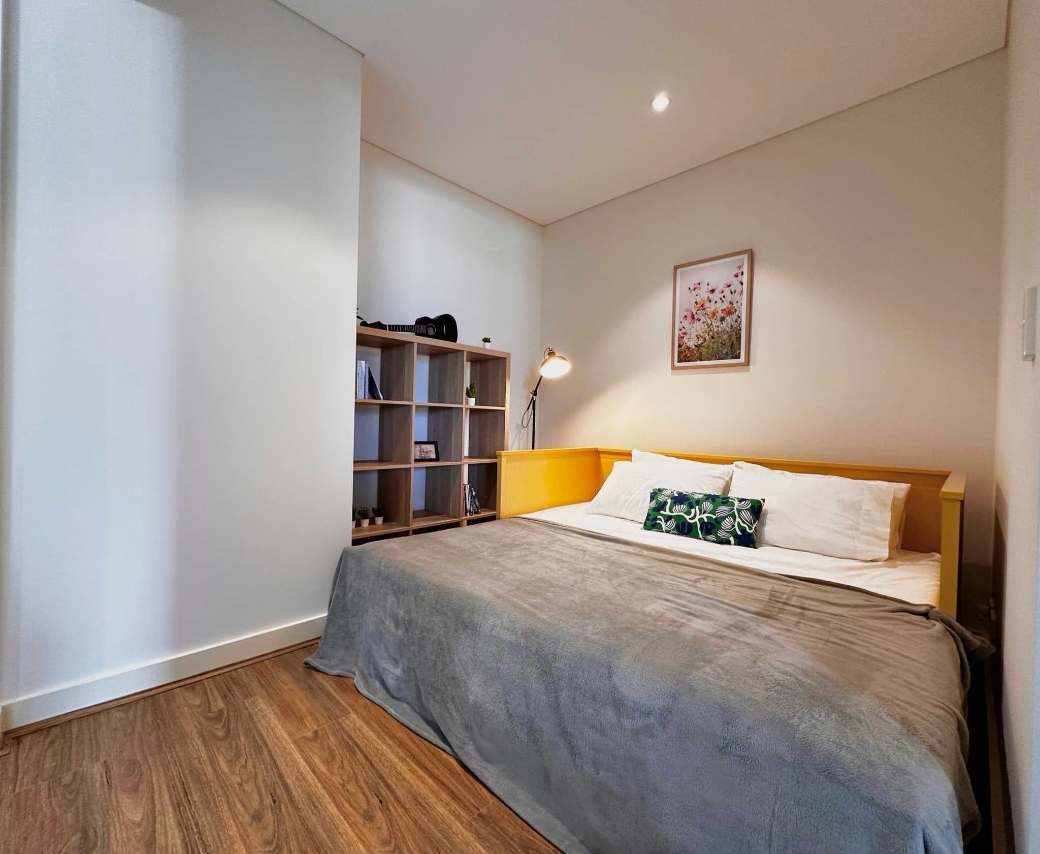 A bedroom with a bed, a wooden wardrobe, and a wall-mounted picture.