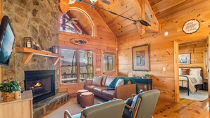 A cozy cabin interior with a stone fireplace, wooden walls, a leather sofa, and a ceiling fan. - Mountain Views, Dog friendly, Fenced Yard, Barrel Sauna, Hot Tub, Fire Pit
 (Ellijay)
