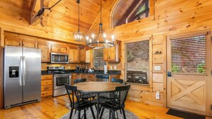 A wooden cabin kitchen with a central island, stainless steel appliances, and a chandelier. - Mountain Views, Dog friendly, Fenced Yard, Barrel Sauna, Hot Tub, Fire Pit
 (Ellijay)