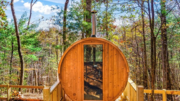 A wooden cabin with a circular door, surrounded by a wooden deck and forest. - Mountain Views, Dog friendly, Fenced Yard, Barrel Sauna, Hot Tub, Fire Pit
 (Ellijay)