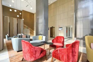 Una hall moderna con un'area salotto caratterizzata da sedie rosse e gialle, un divano grigio e un piccolo tavolino rotondo.