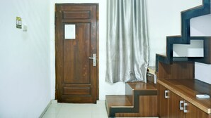 A room with a wooden door, a window with blinds, a curtain, and a wooden desk with drawers.