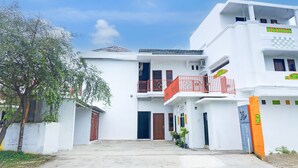 A white two-story building with a balcony, a door, and a small garden area.