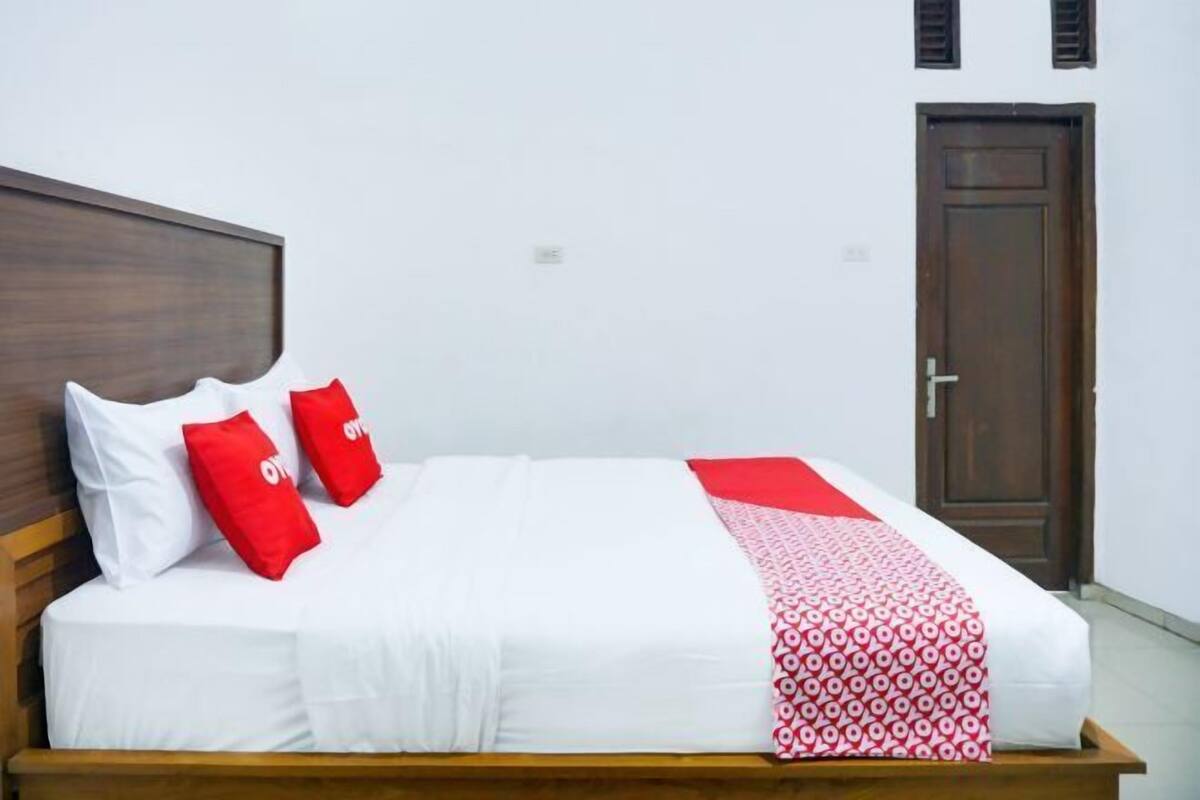 Uma cama com roupa de cama branca, almofadas vermelhas, um cobertor estampado e cabeceira de madeira.