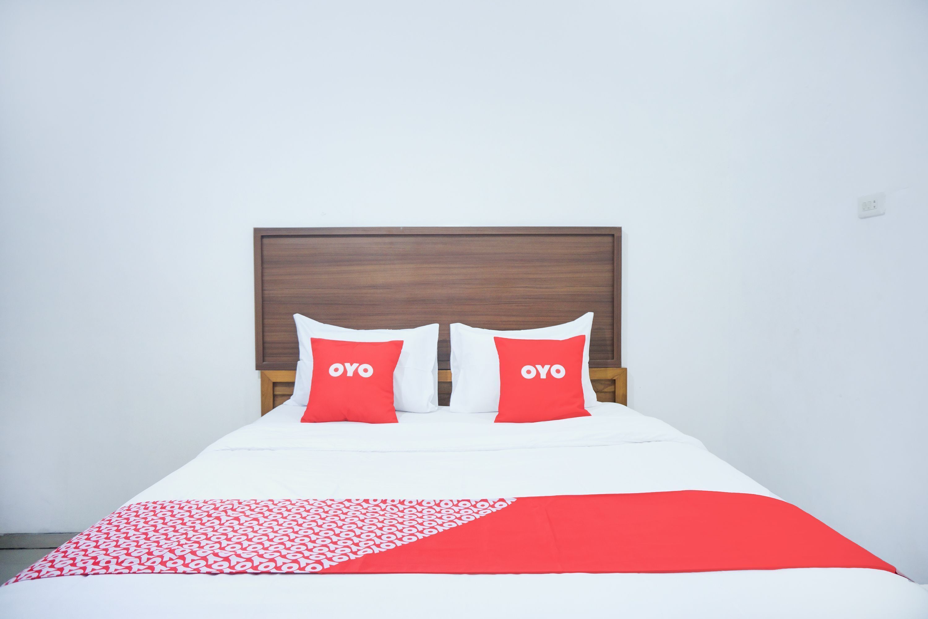 A bed with a white and red bedspread, two red pillows with "OYO" text, and a wooden headboard.