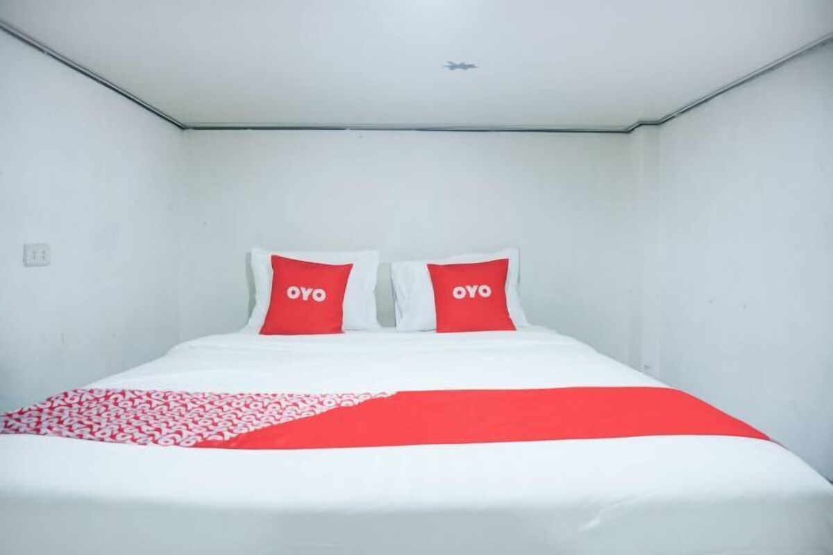 A single bed with white bedding and red accents, two pillows with 'OYO' branding, and a red and white patterned throw.
