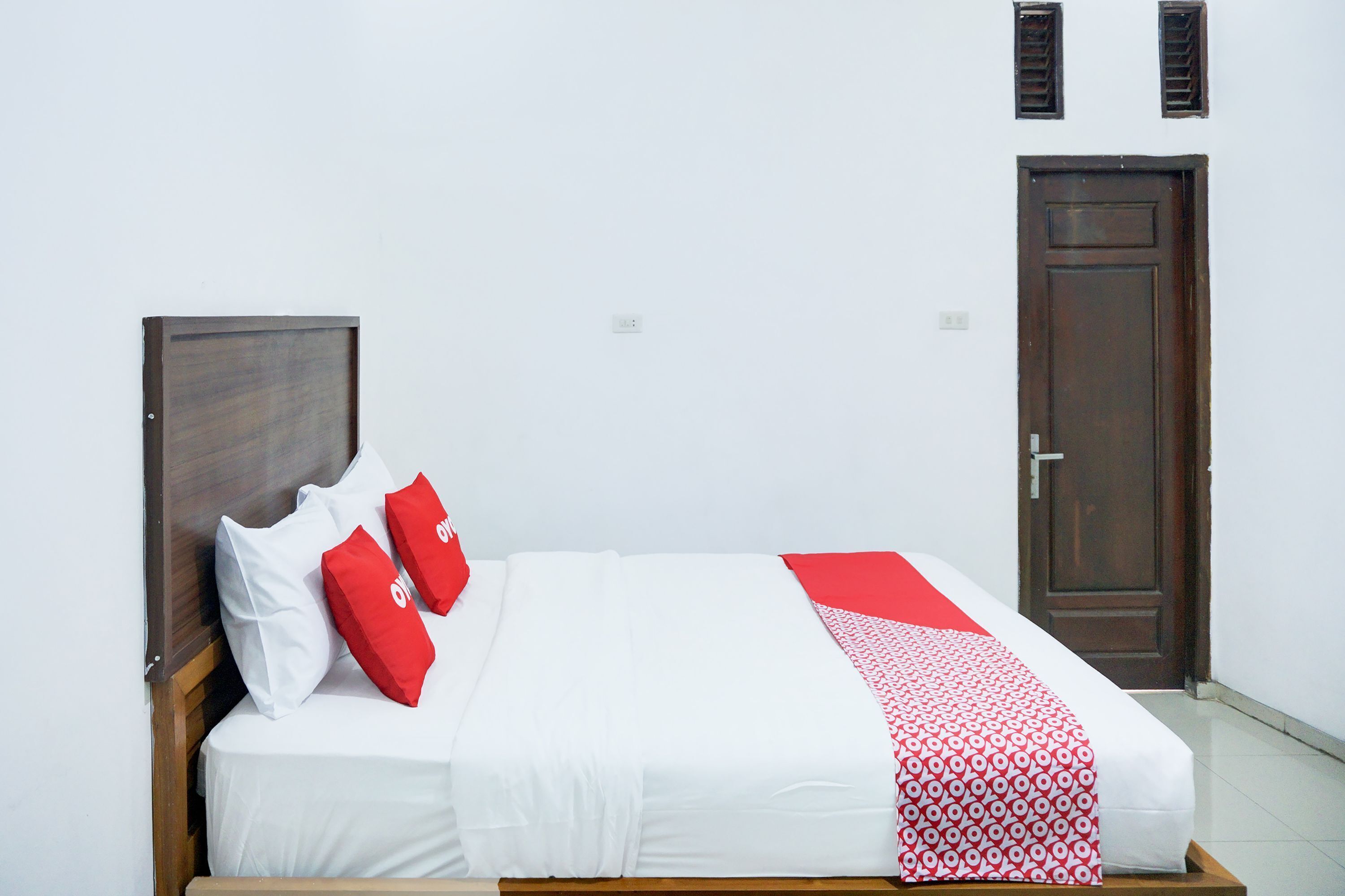 A single bed with white bedding and red accents, a wooden headboard, and two doors in the background.