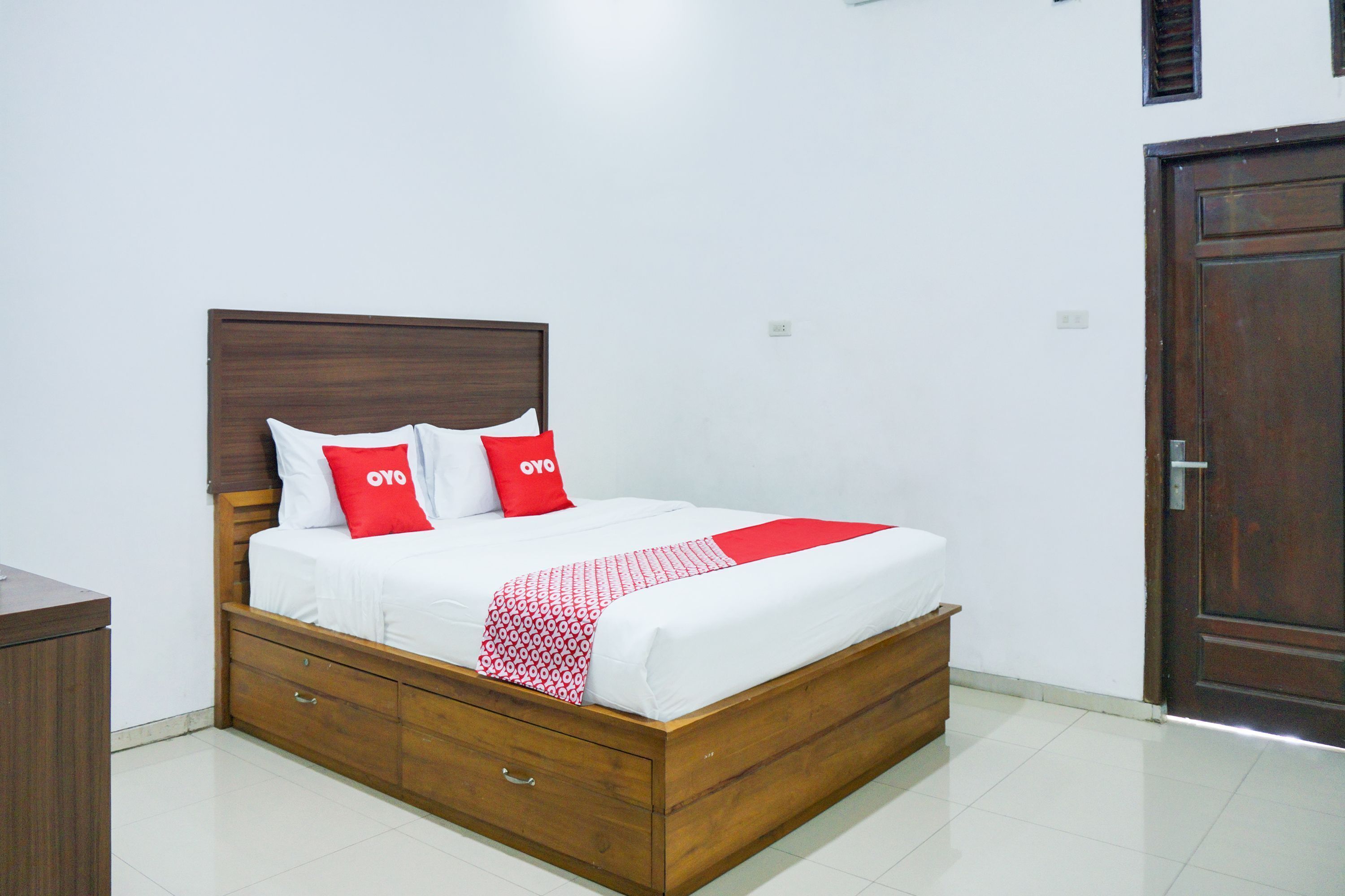 Una cama bien hecha con cabecera de madera, ropa de cama blanca y dos almohadas rojas con el texto "oyo".