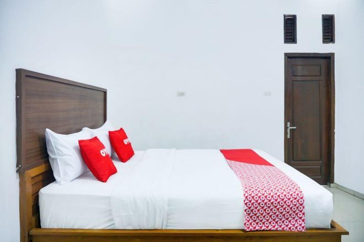 A bed with a wooden headboard, white bedding, and red pillows.