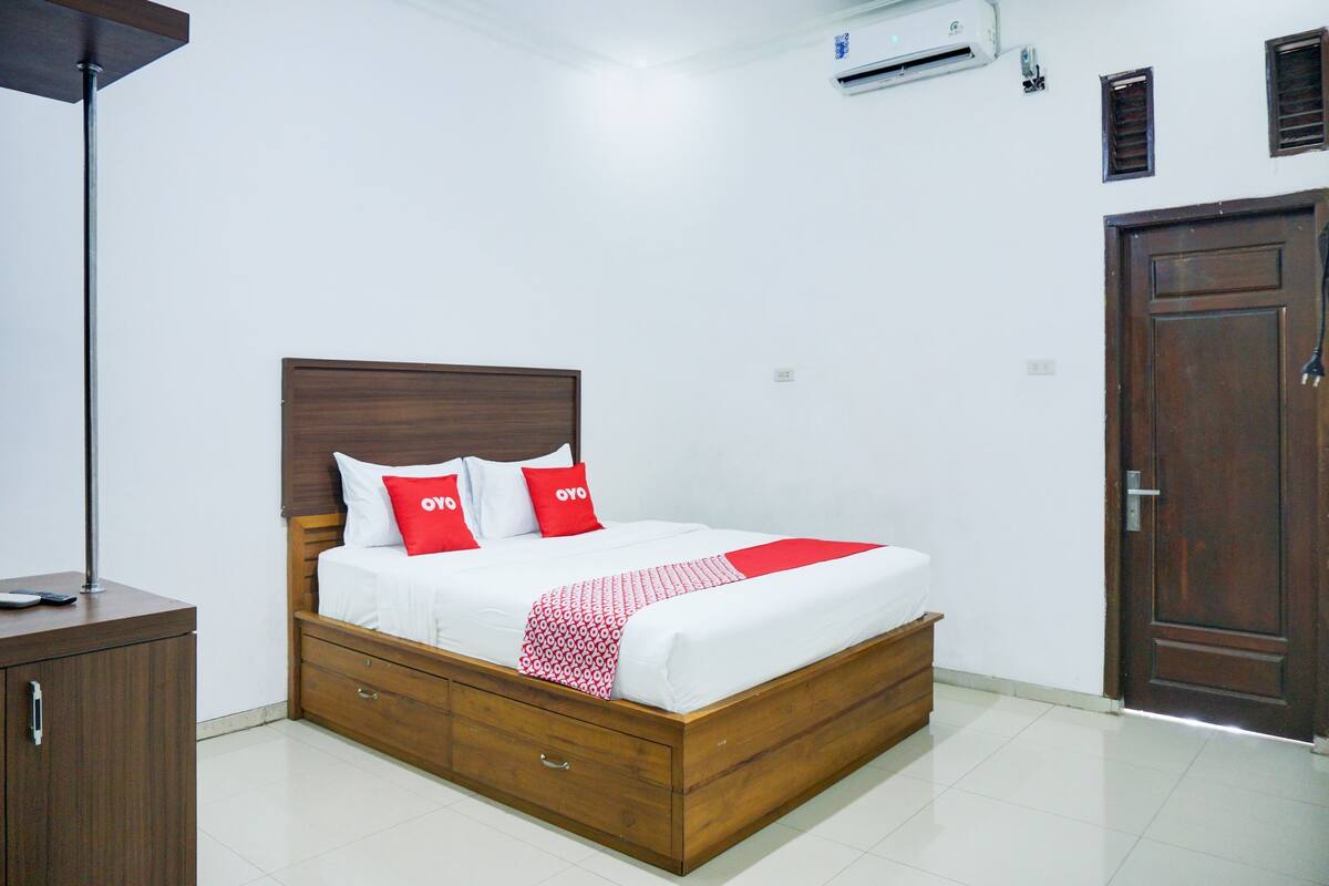 Quarto bem organizado com cama de madeira, roupa de cama branca e manta vermelha.