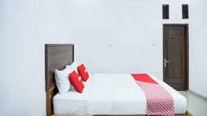 A neatly made bed with white and red bedding, a wooden headboard, and a red and white patterned throw.