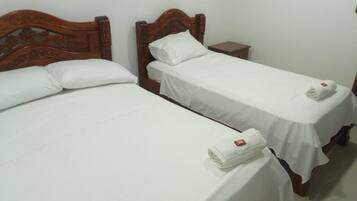 Two single beds with wooden headboards, white linens, and a small nightstand with a lamp.