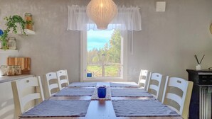 Un comedor con una mesa de madera larga, sillas blancas y vistas a un jardín a través de una ventana.