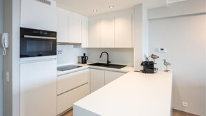 Een moderne keuken met witte kastjes, een ingebouwde oven, een spoelbak en een koffiezetapparaat.
