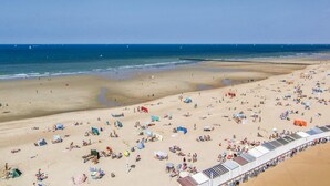 Een strand met veel ligbedden en parasols, een zandstrand en een helderblauwe lucht.