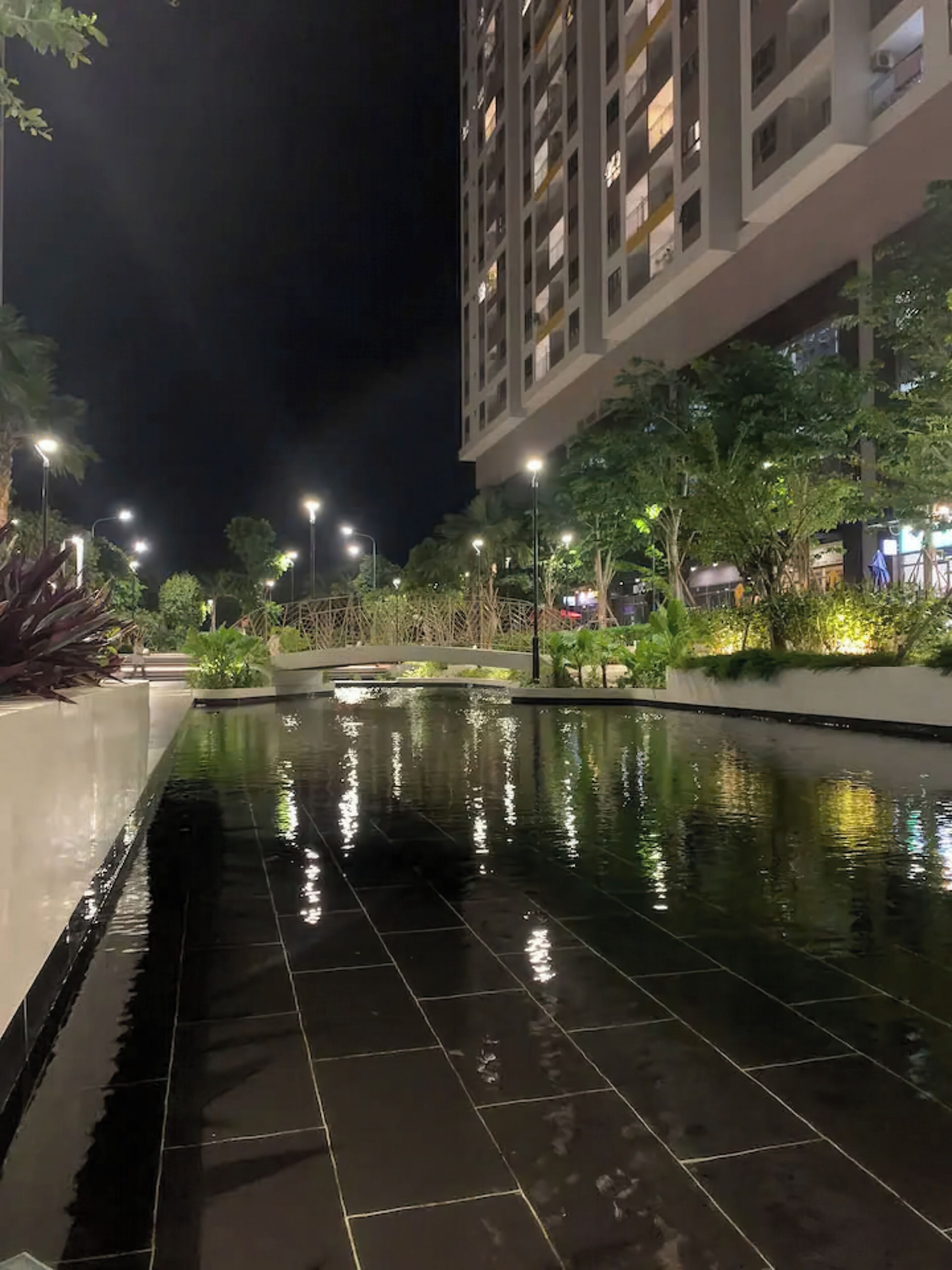 A nighttime view of a modern building with a reflective pool and street lamps.