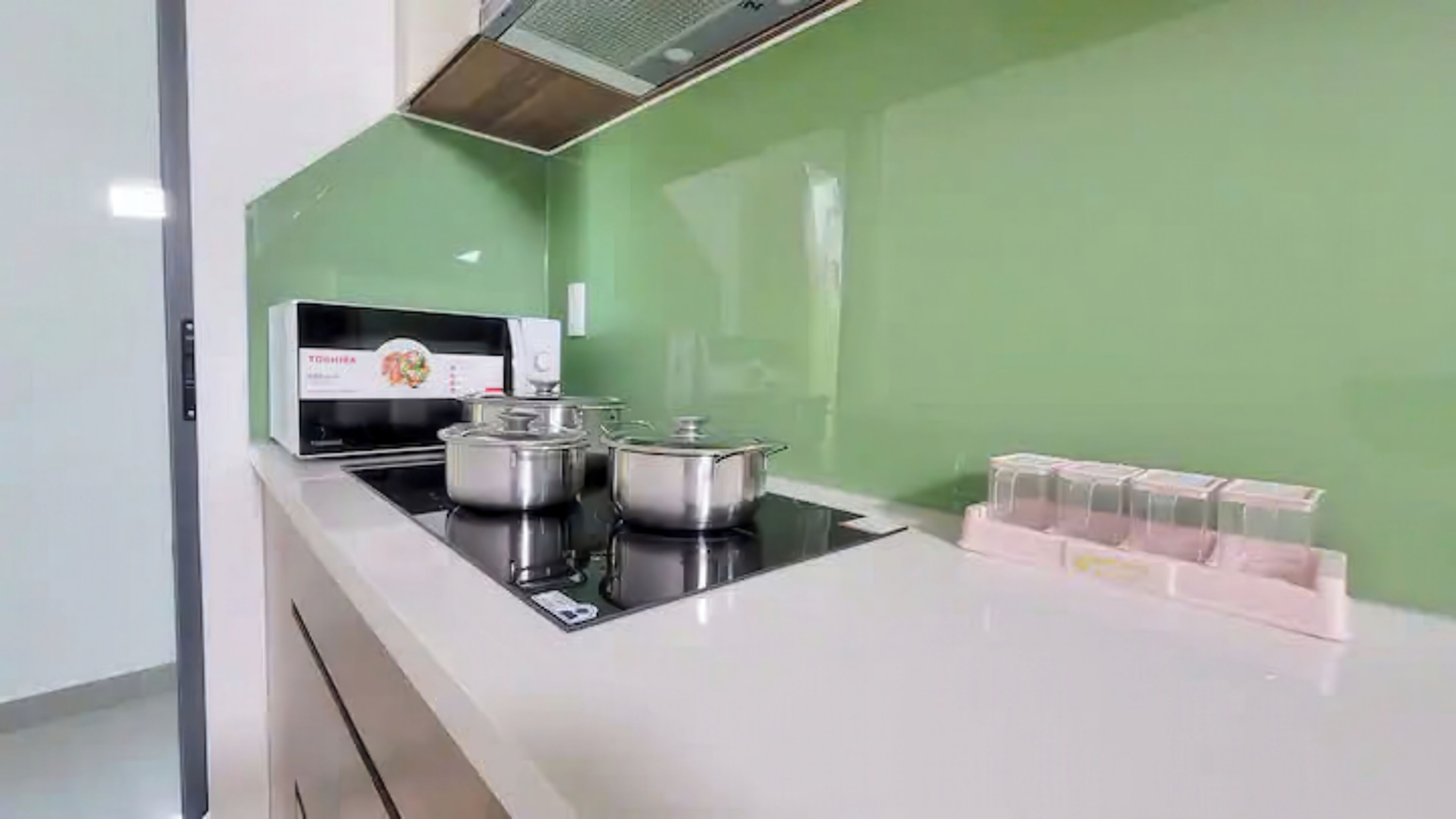 Een keuken met een Toshiba magnetron, twee roestvrijstalen pannen en een set plastic bakjes op het aanrecht.