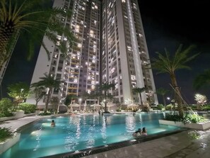 Vue nocturne d’un immeuble de grande hauteur, avec une piscine en premier plan.