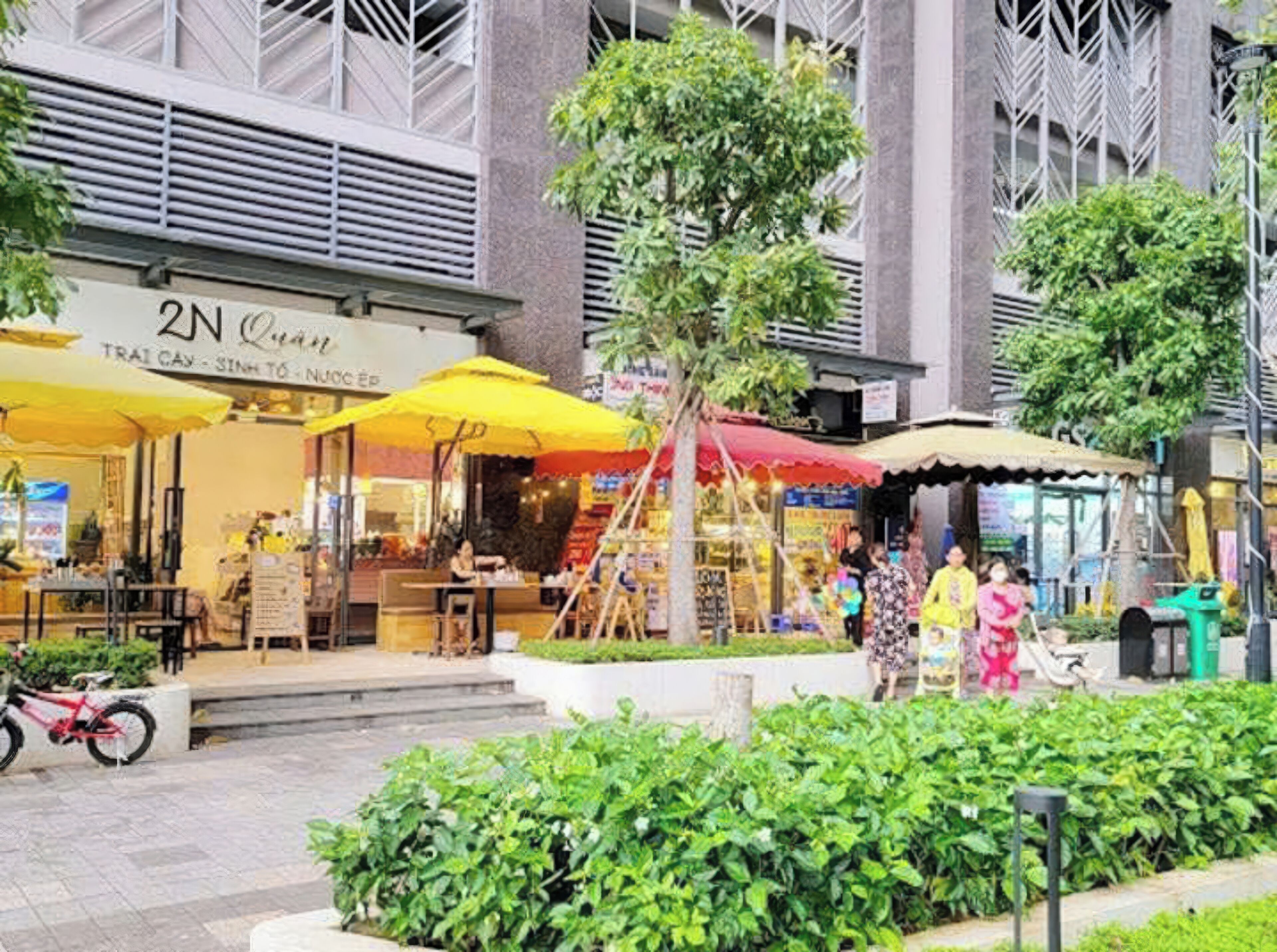 A street scene with outdoor seating at a restaurant, a bicycle, and greenery.