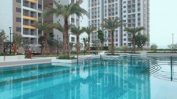 A swimming pool with a tiled deck, surrounded by palm trees and modern buildings in the background.