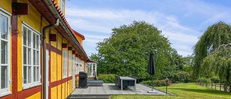 A yellow building with red accents, a covered outdoor seating area, and a well-maintained lawn.