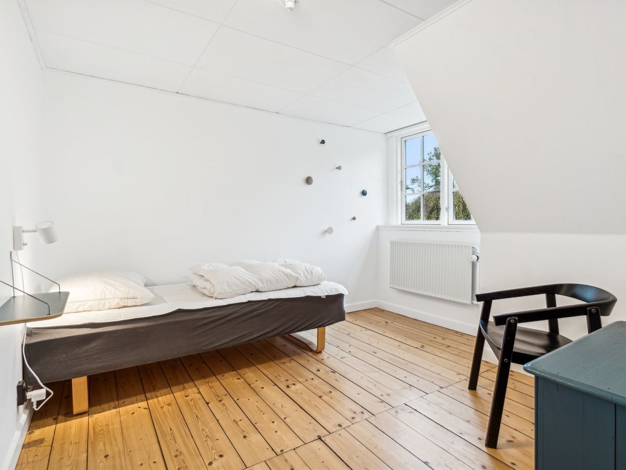 A small, modern bedroom with a sloped ceiling, a bed, a desk, and a chair.