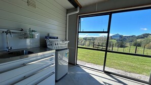 A modern kitchen with a large window, a built-in washing machine, and a view of a green landscape.