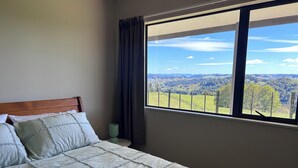 A bedroom with a bed, a view of the countryside through a window, and a neatly made bed with a rolled towel.