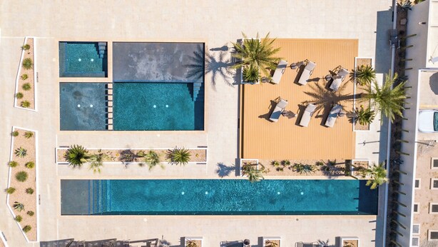 Oversigtsbillede af et resort med flere swimmingpools, liggestole og palmer.