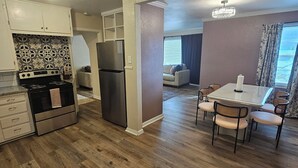 A modern kitchen with a stove, refrigerator, and white cabinets. There is a dining area with a table and chairs. - Isolated King bed, 2 Queen beds - Fenced yard - 9 min to Texas Tech (Lubbock)