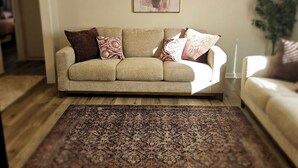 A living room with a beige sofa, patterned cushions, a large rug, and a ceiling fan. - Isolated King bed, 2 Queen beds - Fenced yard - 9 min to Texas Tech (Lubbock)