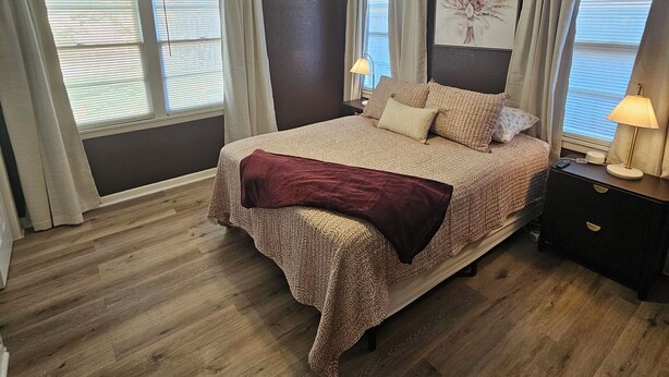 A bedroom with a bed, a ceiling fan, a nightstand with a lamp, and a window with curtains. - Isolated King bed, 2 Queen beds - Fenced yard - 9 min to Texas Tech (Lubbock)