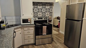A compact kitchen with white cabinets, a stainless steel refrigerator, a microwave, and a stove. - Isolated King bed, 2 Queen beds - Fenced yard - 9 min to Texas Tech (Lubbock)
