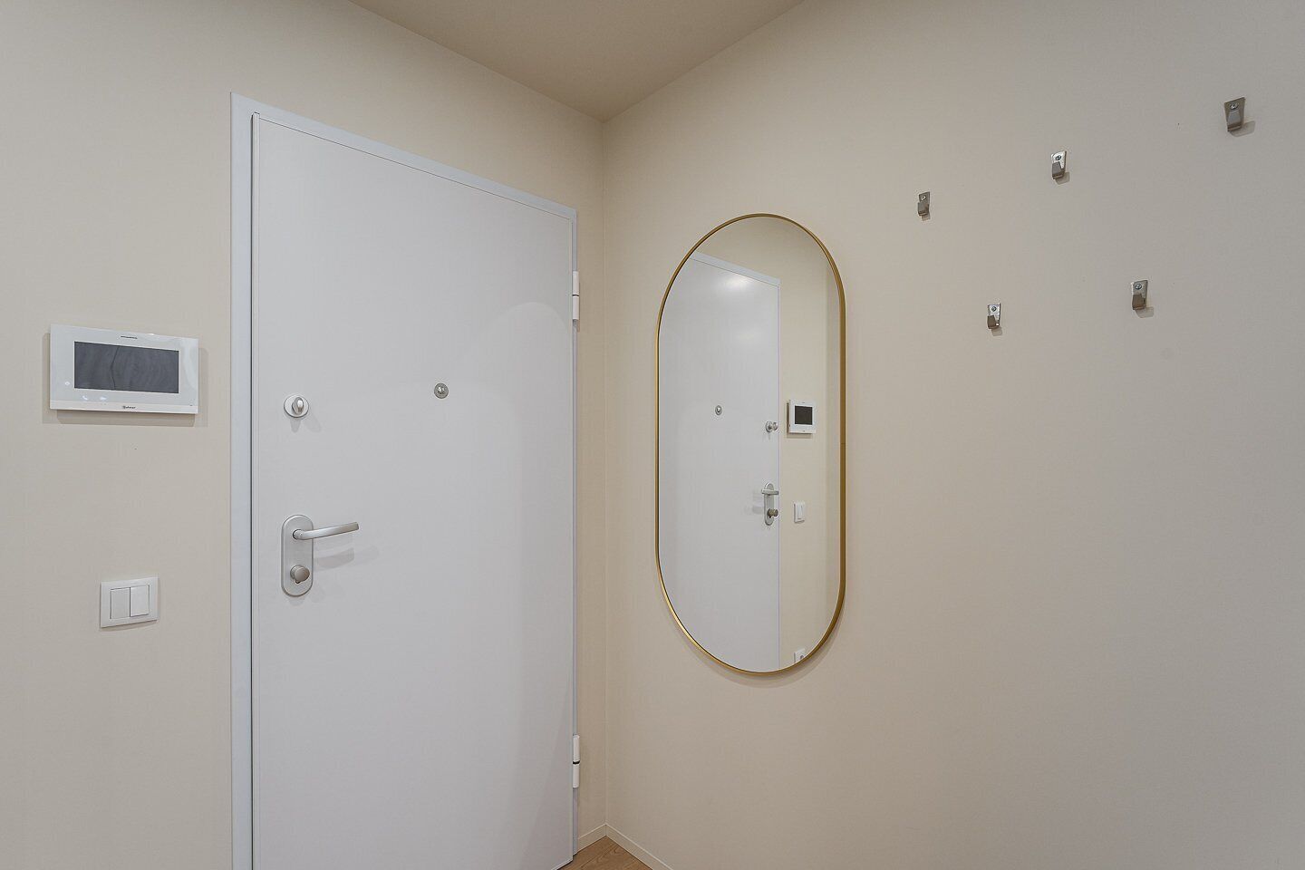 A room with a white door, a wall-mounted TV, a mirror, and a thermostat.