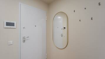 A room with a white door, a wall-mounted TV, a mirror, and a thermostat.