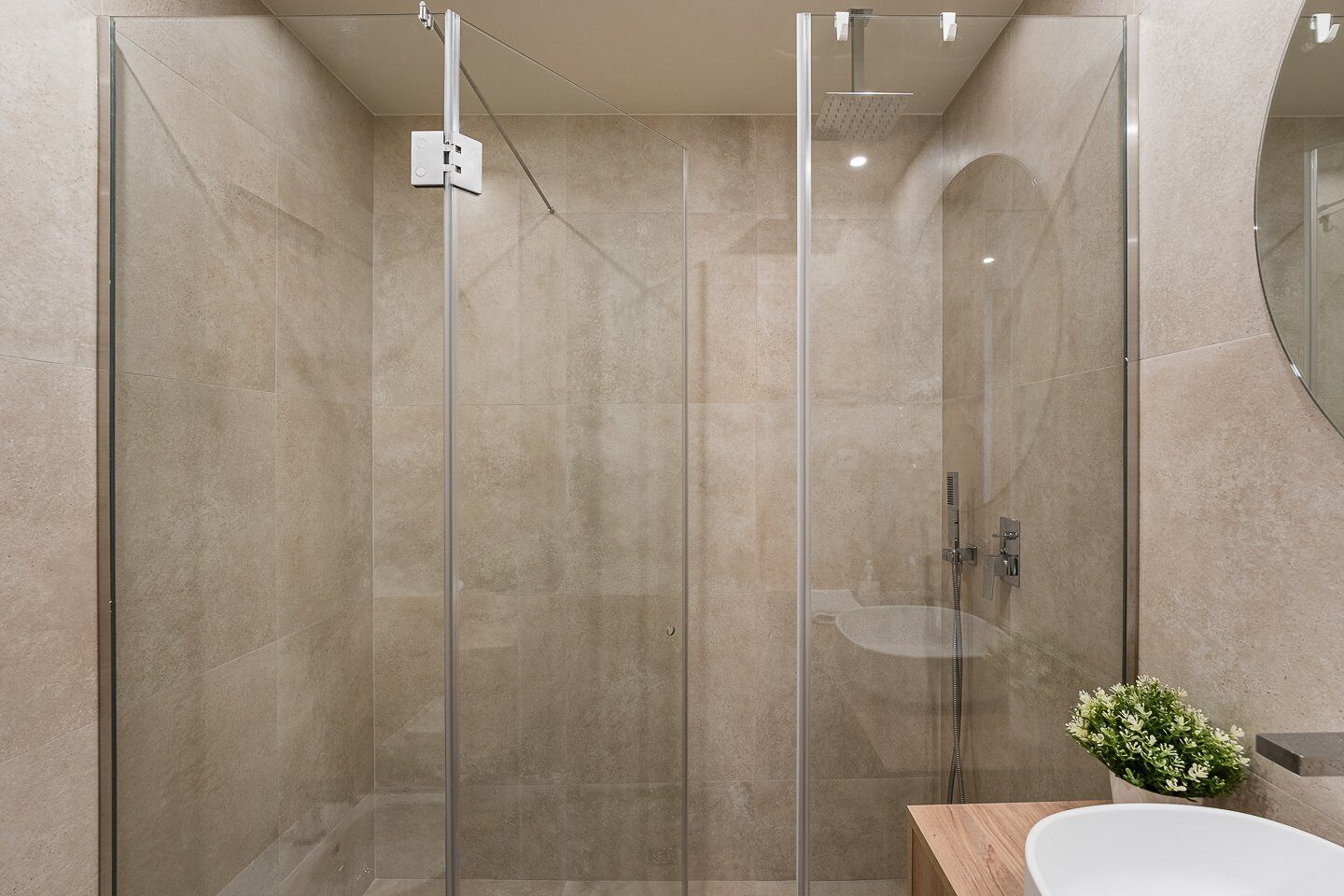 Un baño moderno con ducha de vidrio, tocador de madera y lavamanos blanco.