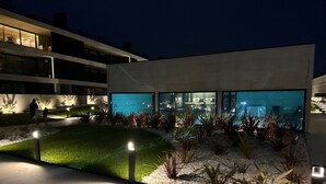 Ein modernes Gebäude mit Glasfassade, einem angelegten Garten und einem Poolbereich.