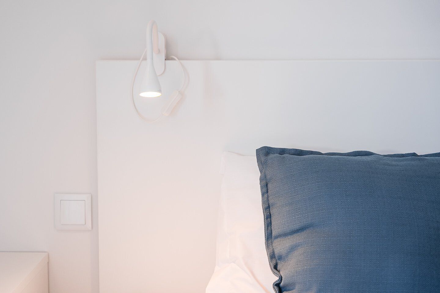 A bedroom with a white headboard, a blue pillow, and a wall-mounted light fixture.