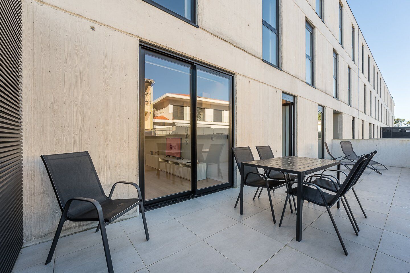 An outdoor patio with a table and chairs, a glass door leading to a building interior, and a clear sky.