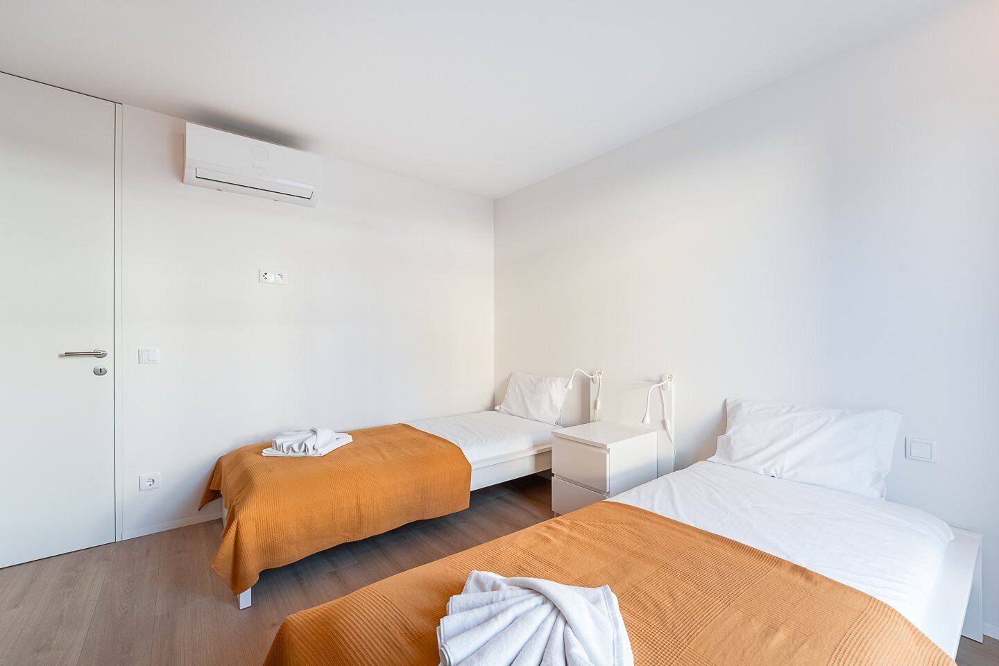 Ein Hotelzimmer mit zwei Betten, einem Kleiderschrank, einem Nachttisch und einer Klimaanlage.