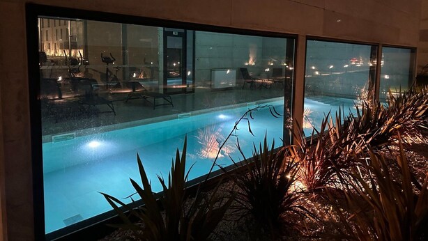 Ein moderner Poolbereich im Innenbereich mit Glaswänden, Liegestühlen und einem sichtbaren Eingang.