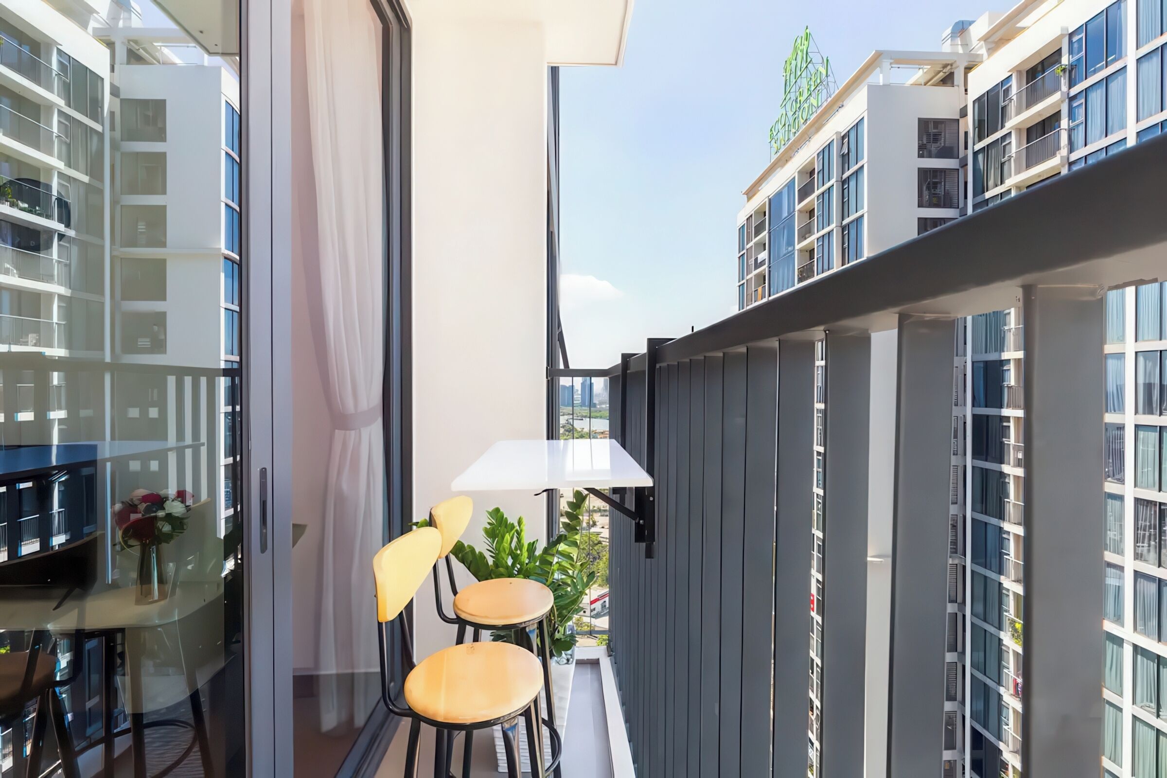 A balcony with a table and chairs, a potted plant, and a view of neighboring buildings.