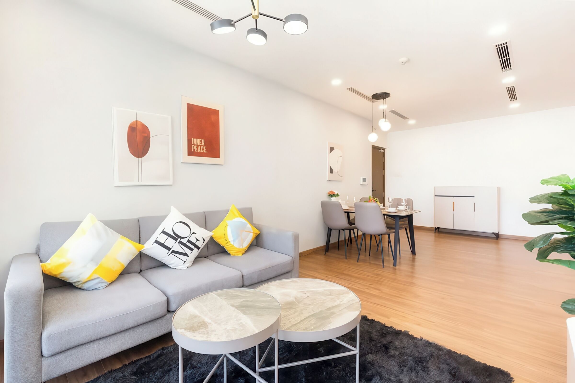 Una sala de estar moderna con un sofá gris, dos mesas redondas y una zona de comedor con sillas y una mesa.