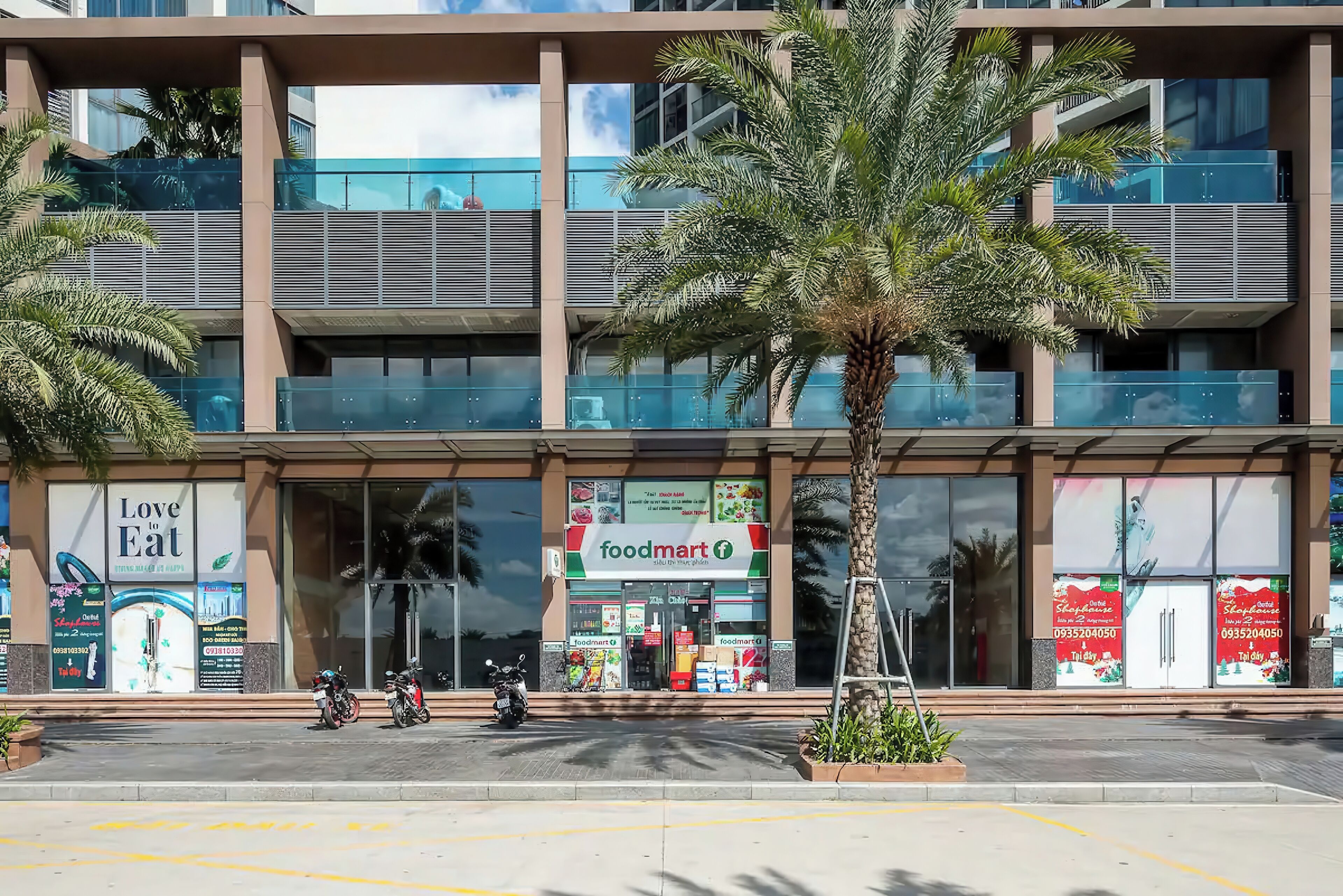 A modern building with a Foodmart store on the ground floor, featuring large glass windows and a palm tree in the foreground.