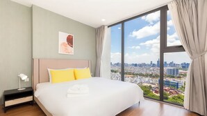Una habitación de hotel moderna con una cama grande, una mesita de noche, una lámpara y vistas a la ciudad a través de amplias ventanas.