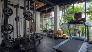 A gym with weightlifting equipment, a treadmill, and large windows with a view of greenery. - Sacred Valley by GenuineHost (Sebatu)