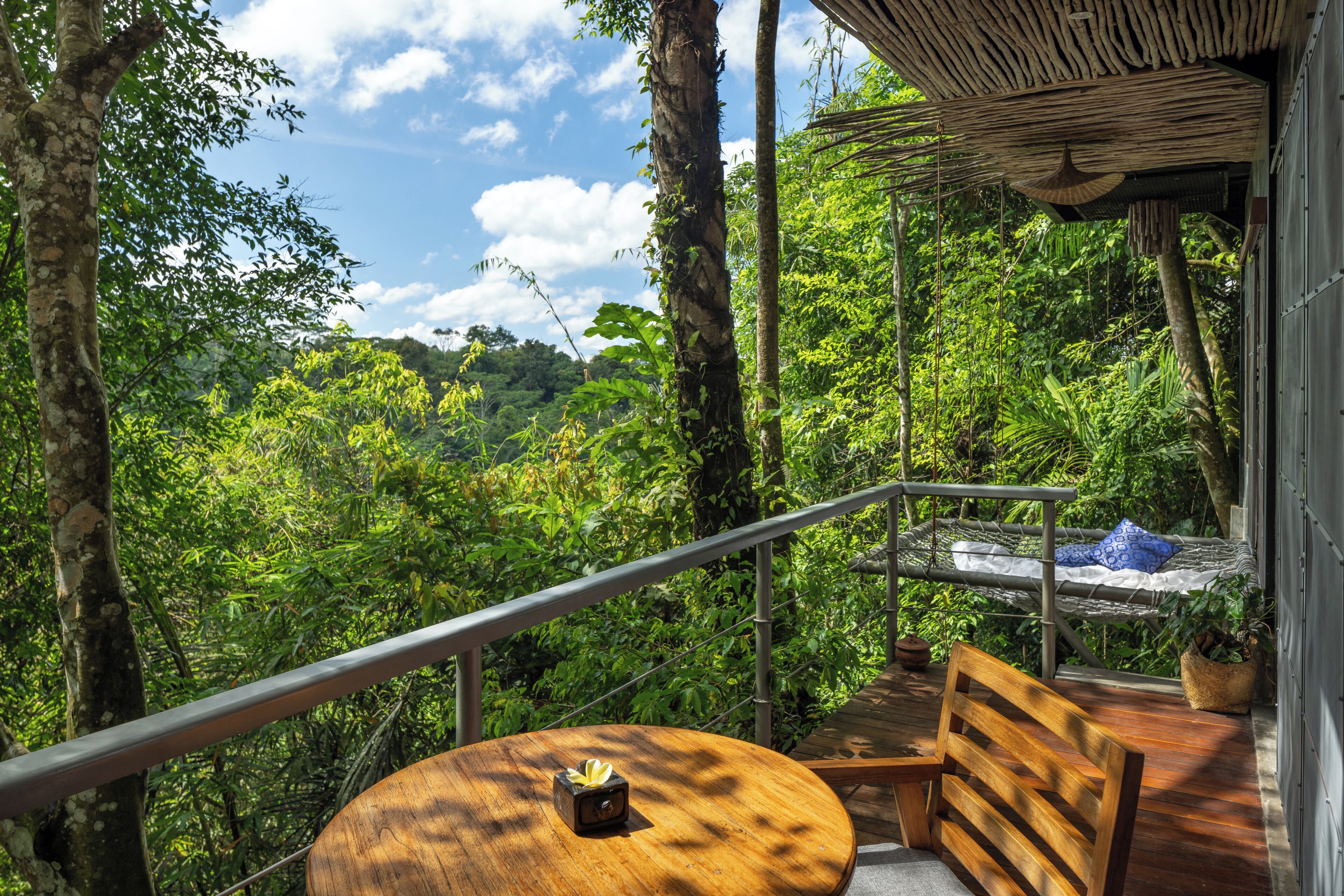 A wooden deck with a round table and a bench, overlooking a lush forest.